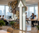 Office workspace with large gears wall decoration and illuminated arrows, people working at desks with laptops
